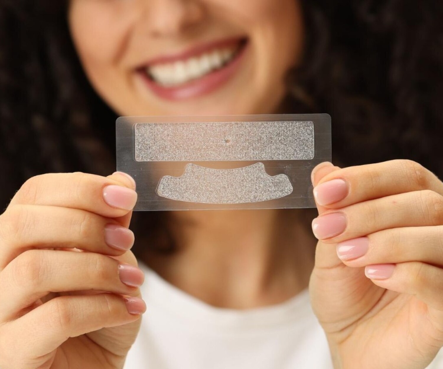 Close-up of a woman holding a teeth whitening strip with a bright smile.