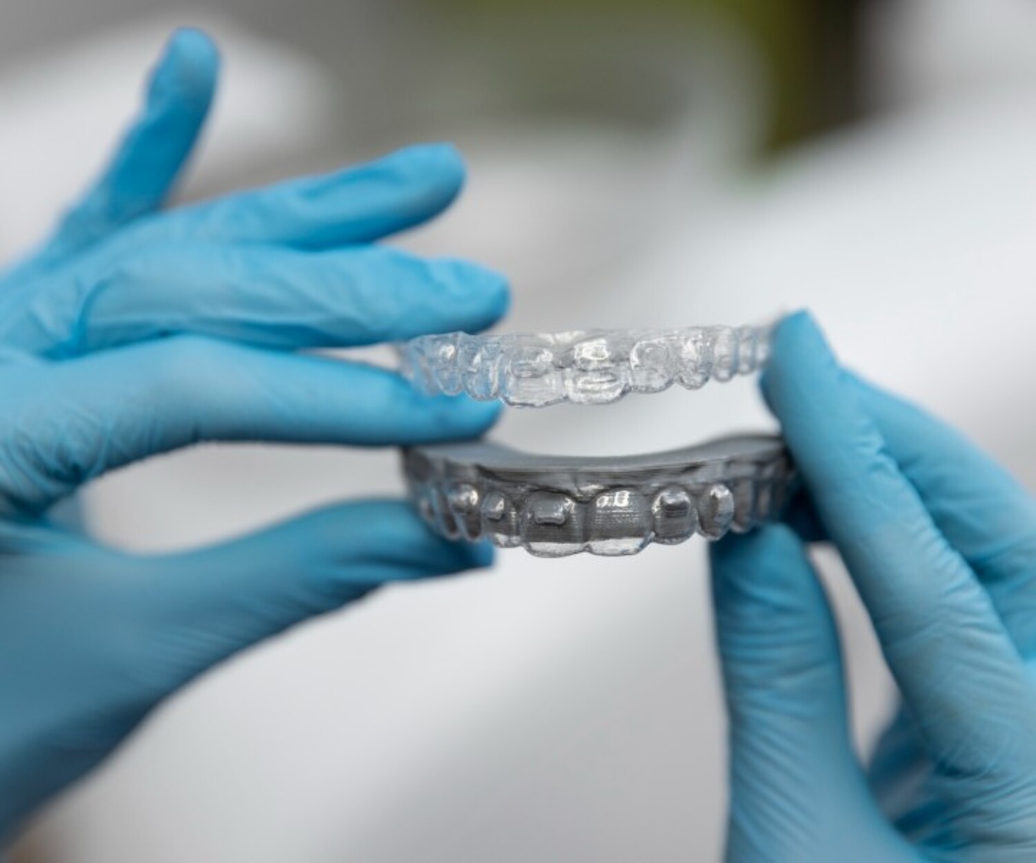 Clear dental aligners held by a gloved dental professional.
