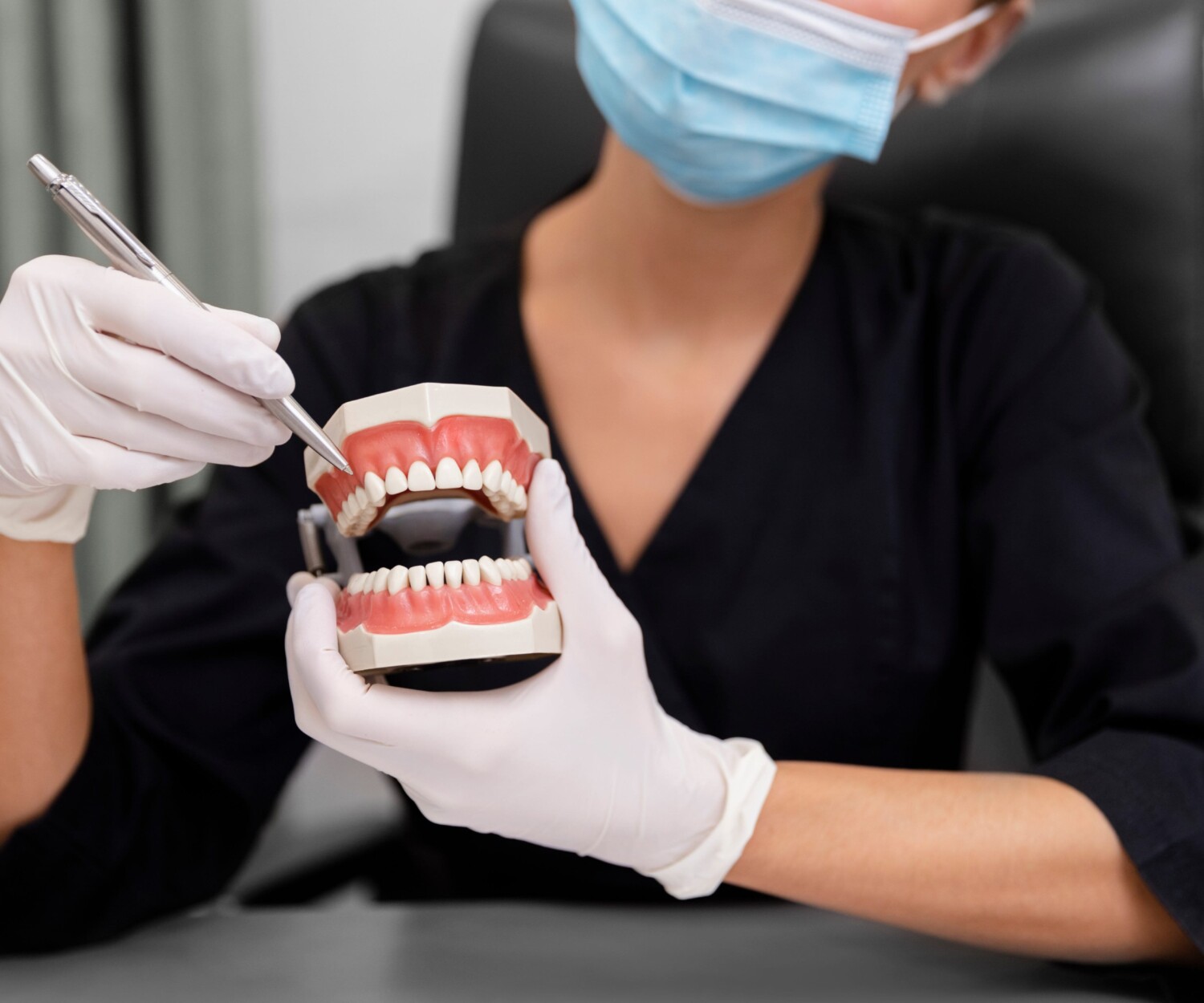 A dentist holding a dental model and pointing to teeth with a pen.