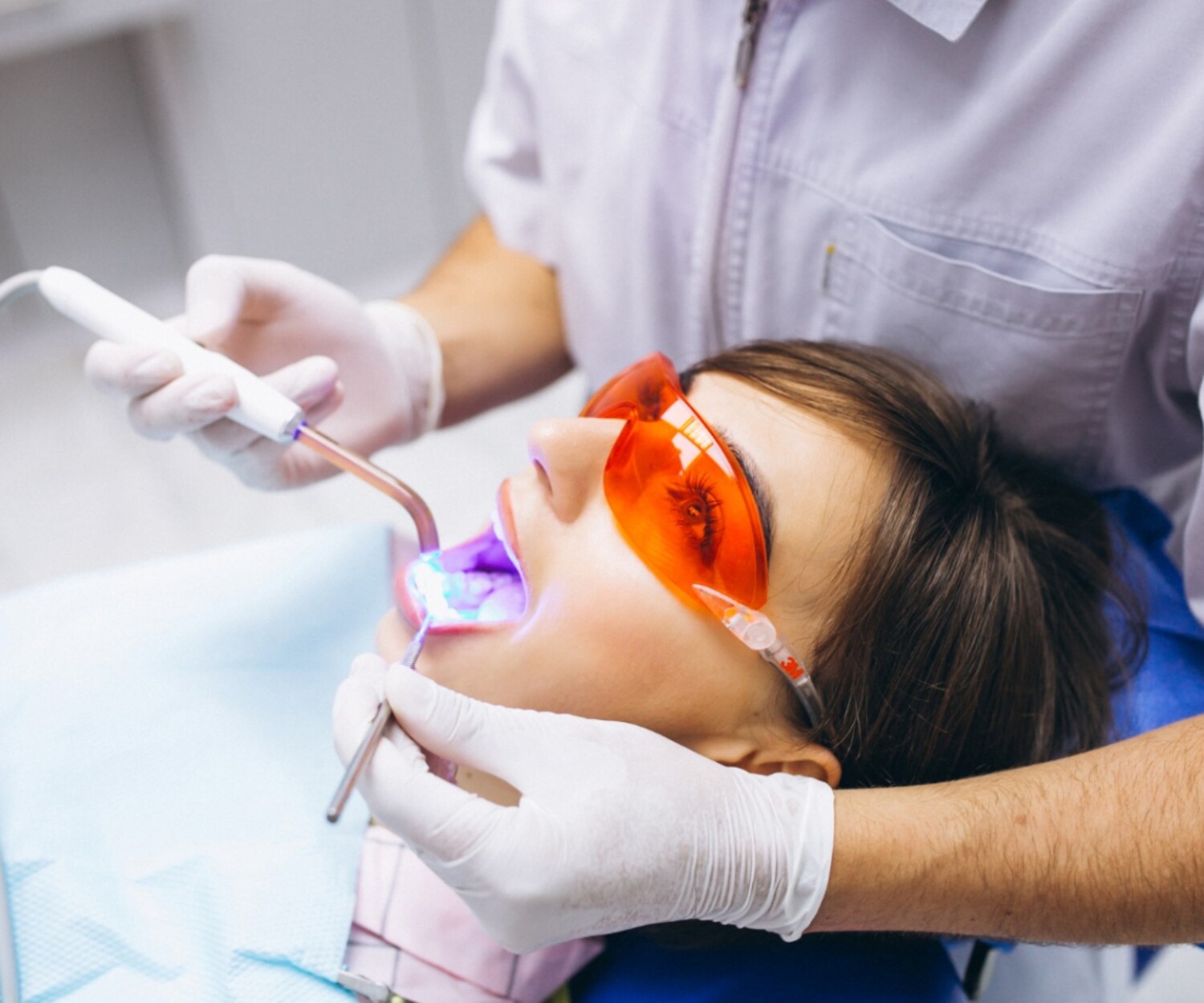 Dentist performing laser teeth whitening treatment with protective eyewear and light-activated system on patient