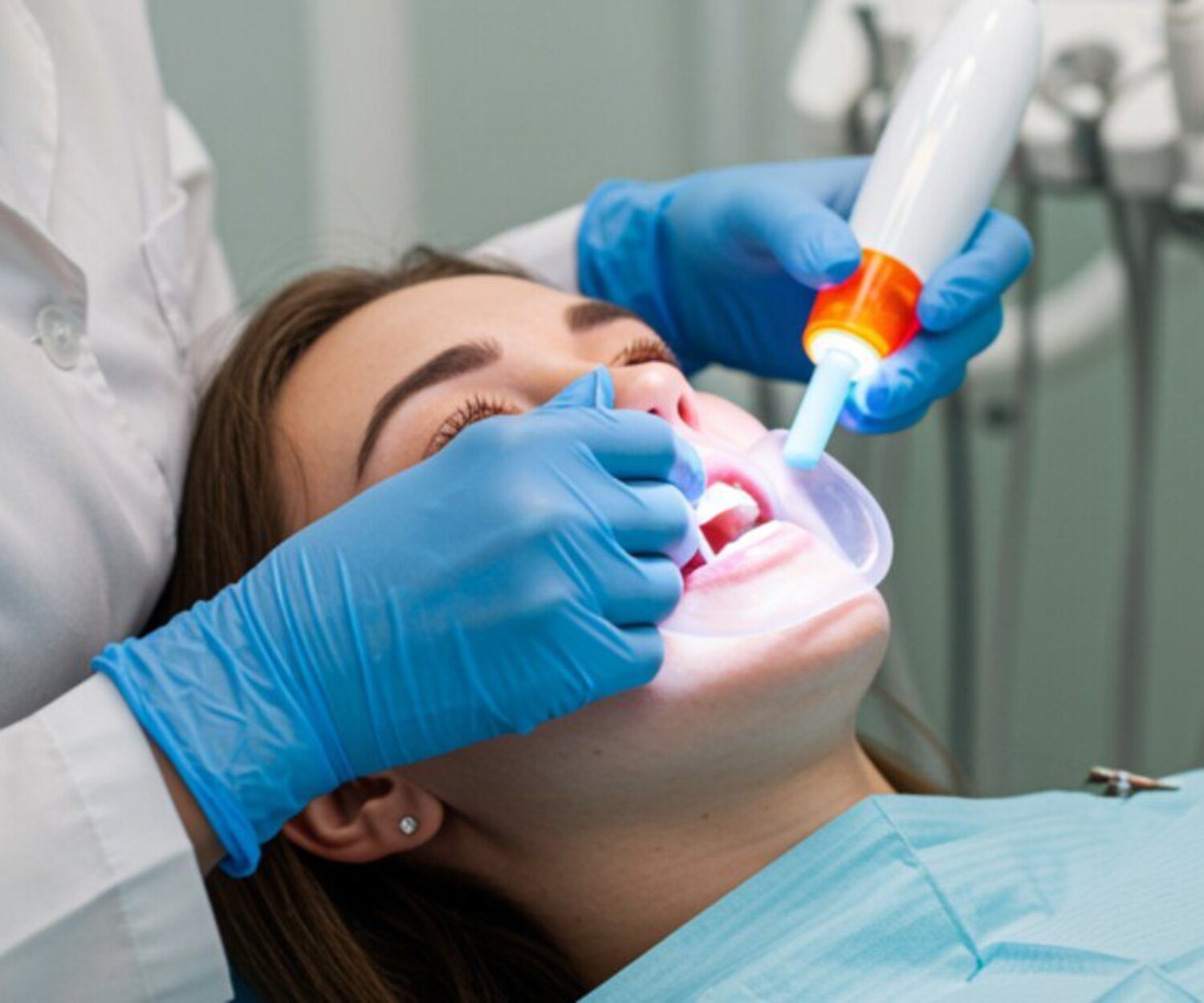 Dentist carefully performing a whitening procedure on a patient using gel and LED light, with protective tools like cheek retractors and gum barriers visible to highlight safety.